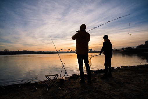 Father and son are fishing on sunny winter day. Freshwater fishing. Teenage boy is learning to fish.