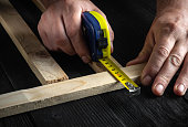 Carpenter uses a construction tape to measure the length of a piece of wood. Hands of the master close-up at work. Working environment in a carpentry workshop.