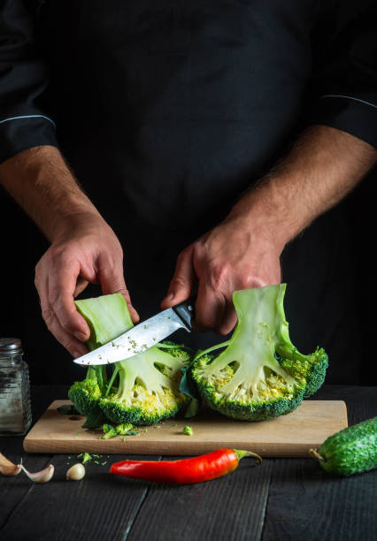 istock Cook cuts fresh Broccoli with a knife for salad on vintage kitchen table with fresh vegetables. Cooking and restaurant or cafe concept 1458742277