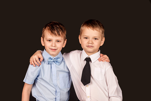 Two smiling happy boys friends in white and blue shirts hugging looking at camera isolated on black background. Fashionable guys school children, studio shot. Childhood concept. Copy text space for ad