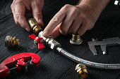 Professional plumber connects brass fittings to plumbing hose. Close-up of hand of the master during work in workshop.