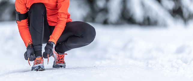 A close-up view of a female runner tying her shoelaces before training on the snow in the winter season.
