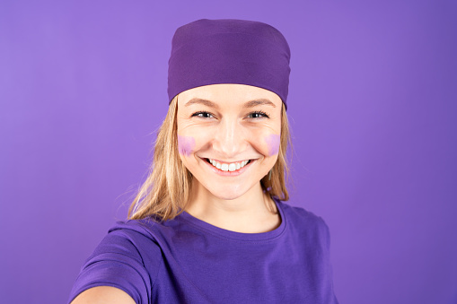 Smiling feminist activist taking selfie isolated on purple background