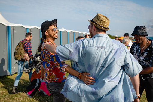 A group of festival goers at a festival in Lindisfarne, North East England walking through a field towards the music. The main focus is a couple walking while they embrace and smile at each other.