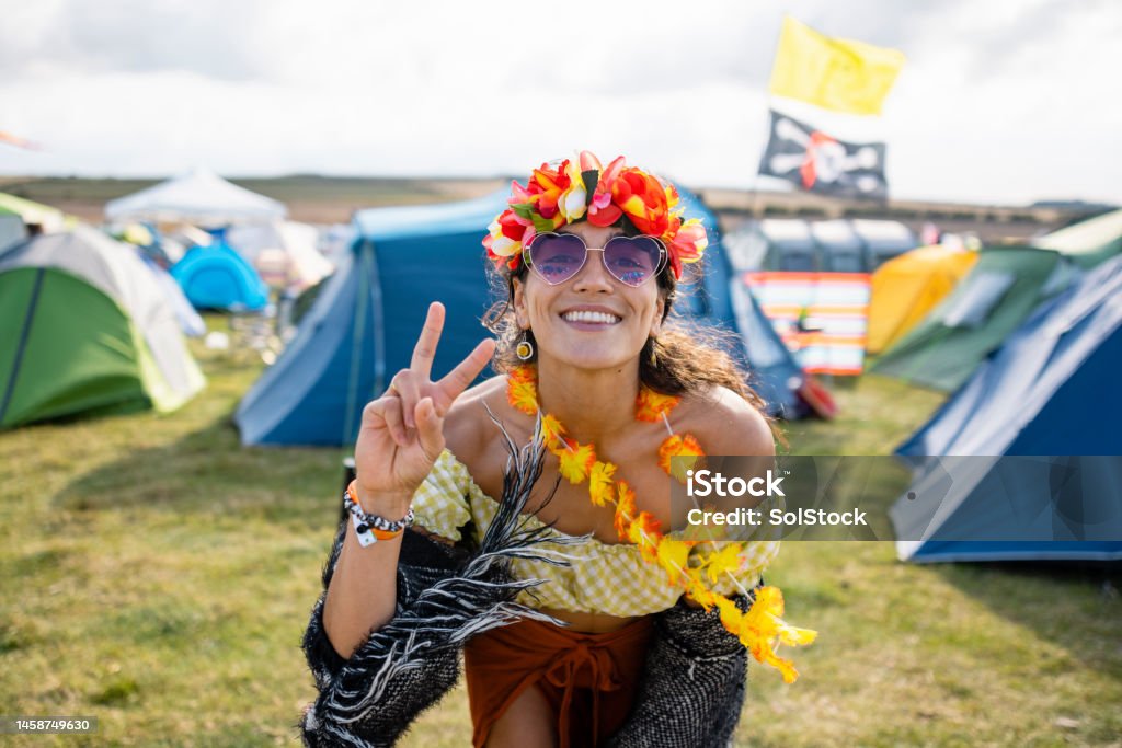 Peace Out Baby A young woman at a festival in Lindisfarne, North East England. She is wearing a flower headband, flower garland and heart sunglasses and doing the peace sign while looking and smiling at the camera. Music Festival Stock Photo