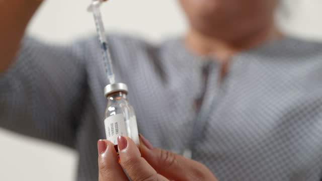 Asian menopausal mature woman wearing glasses holds a syringe and a vaccine bottle