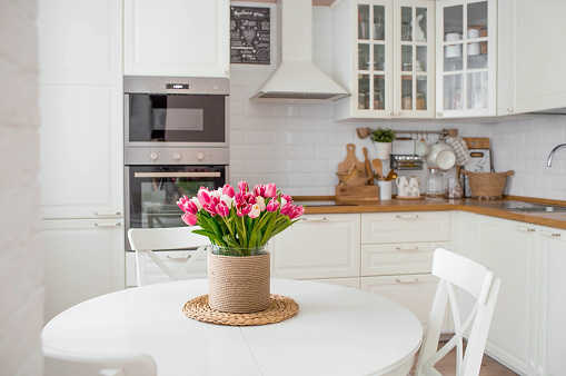 A bouquet of tulips on a white table. In the background, the interior of a white kitchen in the Scandinavian style. The concept of home comfort.The concept of International Women's Day on March 8.