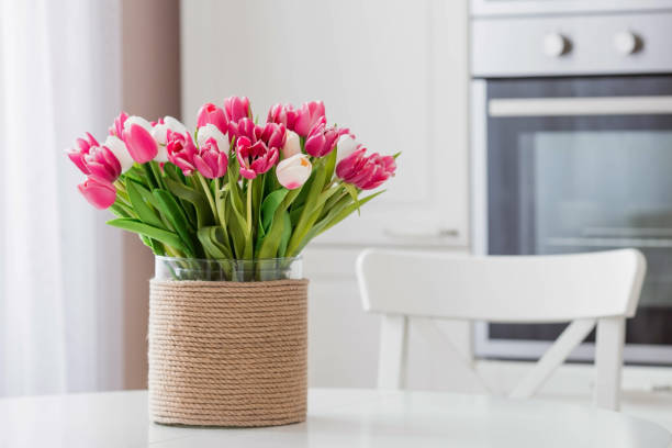 白いテーブルに置かれたチューリップの花束。背景には、スカンジナビアスタイルの白いキッチンのインテリア。家庭の快適さの概念。3月8日の国際女性デーのコンセプト。
