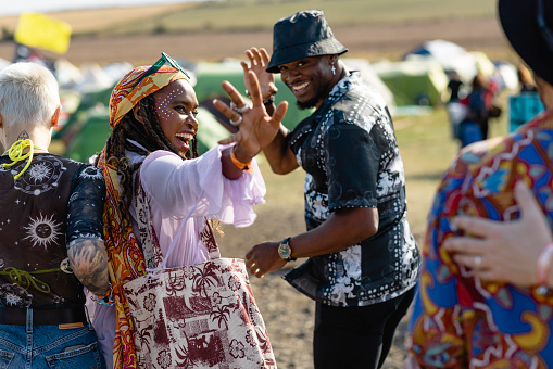 Festival goers walking through a field at a festival in Lindisfarne, North East England. The main focus is two of them looking over their shoulders while waving and smiling.