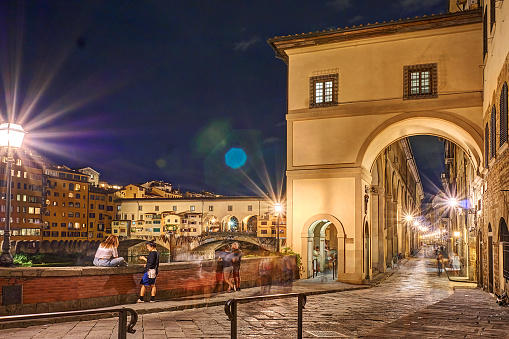 Florence, Italy - September 07, 2022: People at the Lungarno degli Archibusieri at night. In the background, Ponte Vecchio, the symbol of the city.