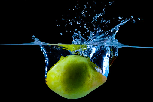 Pear falling underwater with splashes on black.