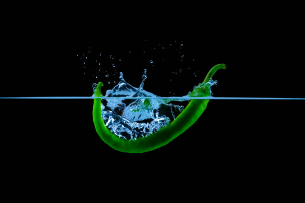 Green chili pepper falling underwater with splashes on black.