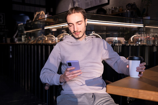 Young man looking at his phone with his drink in cafe