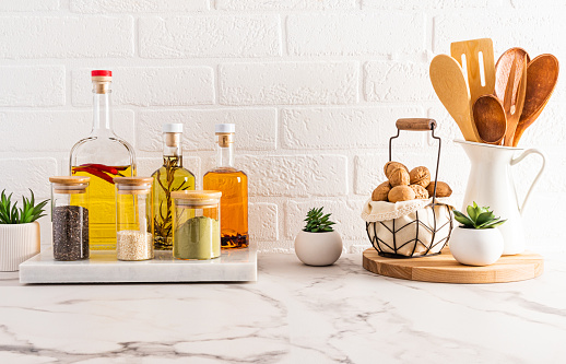 several bottles of butter for cooking and kitchen utensils in the modern kitchen on a white marble countertop. brick wall. front view