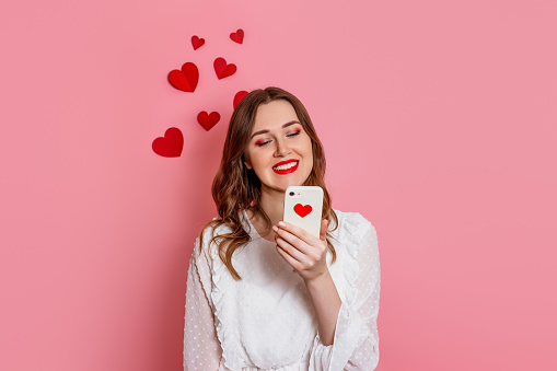 Dating App. The girl reads love sms smiling on a pink background. valentine's day congratulations