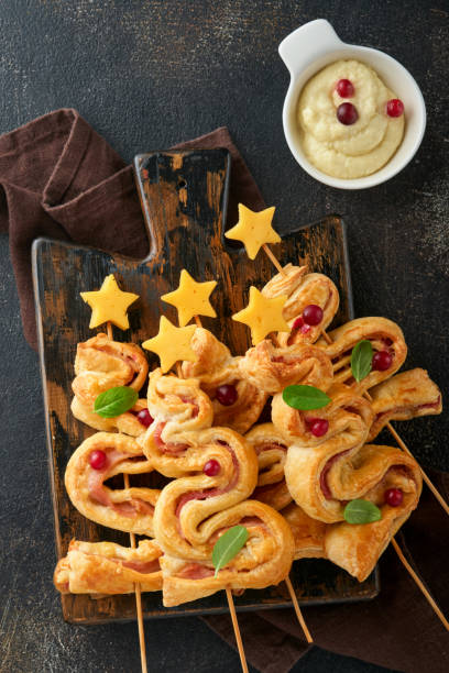 istock Christmas or New Year appetizer. Christmas tree shape puff pastry buns with cheese and ham. Group of Christmas tree shapes on wooden board. Festive idea for Christmas or New Year dinner. Top view. 1458779467
