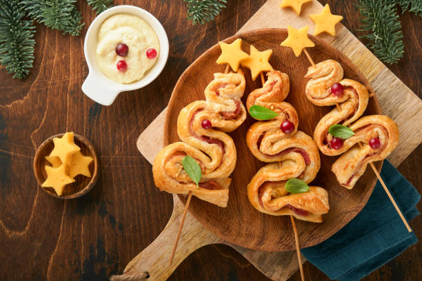 istock Christmas or New Year appetizer. Christmas tree shape puff pastry buns with cheese and ham. Group of Christmas tree shapes on wooden board. Festive idea for Christmas or New Year dinner. Top view. 1458779549