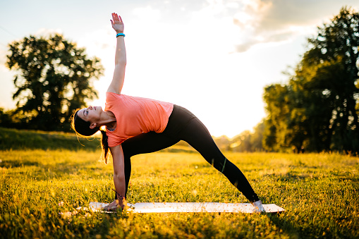 Beautiful young woman doing yoga in the park as the sun sets.