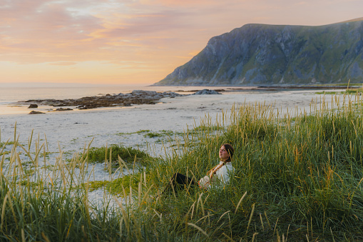 Female with long hair enjoying a day at the beautiful beach with mountain view during summer sunset on Lofoten, Nordland county, Northern Norway