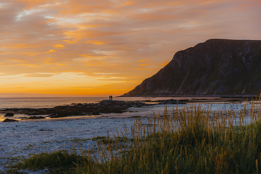 Scenic sunset time with Midnight Sun over the beautiful beach with mountain view and incidental people walking at the coastline in Northern Norway