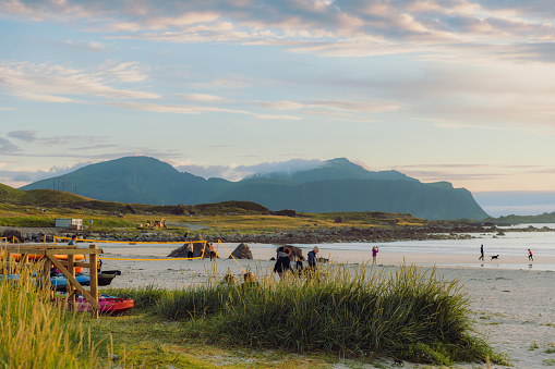 Scenic sunset time with Midnight Sun over the beautiful beach with mountain view and incidental people walking at the coastline in Northern Norway