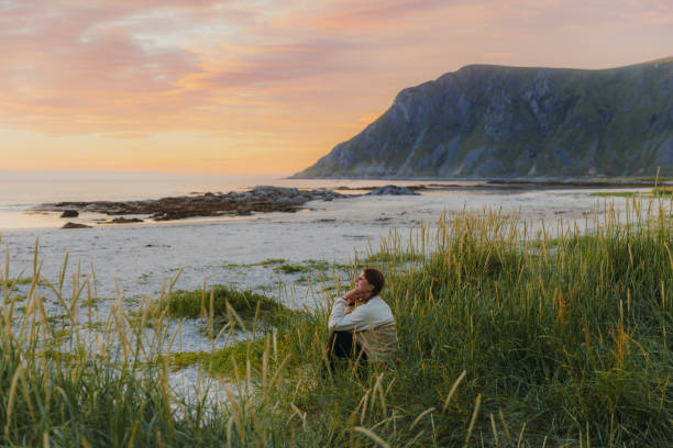 vue latérale d’une voyageuse contemplant le coucher du soleil près de la plage de montagne pittoresque des îles lofoten - norvège septentrionale photos et images de collection