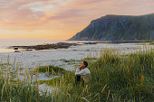 Side view of a woman traveler contemplating sunset by the scenic mountain beach on Lofoten Islands
