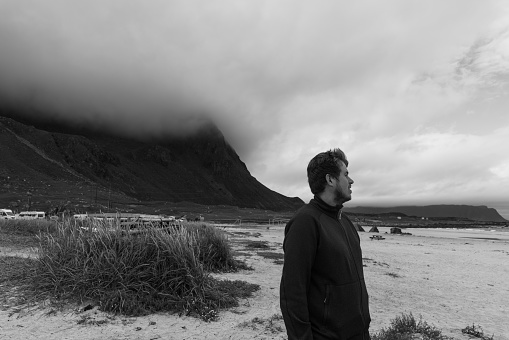 Black-white photo of a happy male traveler enjoying a summer time at the scenic mountain beach on Lofoten, Norway