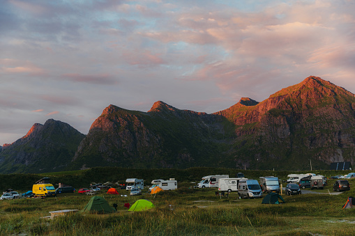 Dramatic shiny mountain peaks and the camping site by the beach during bright sunset