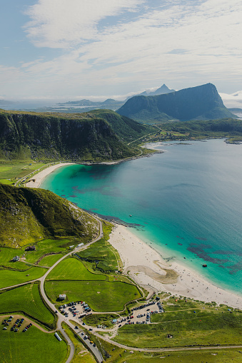 High-angle photo of the scenic landscape with the road, turquoise-colored white sand beach and the mountain peaks on Lofoten, Nordland, Northern Norway