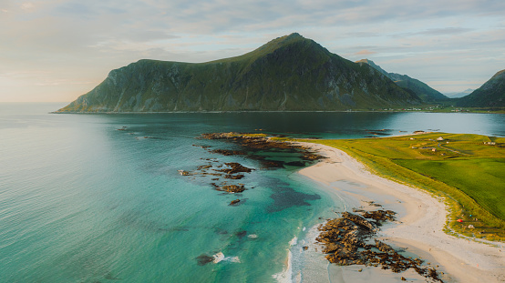 Drone high-angle photo of dramatic summer sunset above the sand beach with a view of the crystal blue ocean and the mountains in Northern Norway