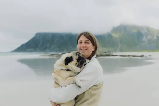 Photo of Happy woman contemplating a beach day on Lofoten Islands walking with her dog