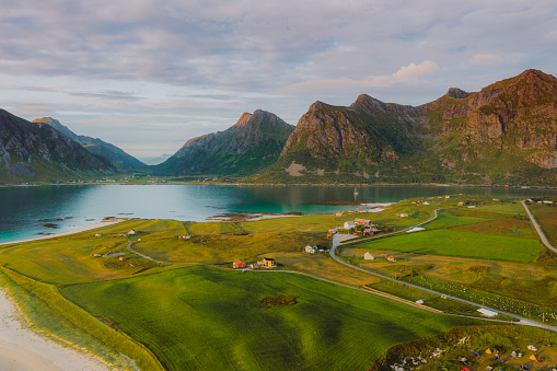 Drone high-angle photo of the old authentic village with view of the beautiful mountain peaks and the sea during bright summer sunset in Northern Norway