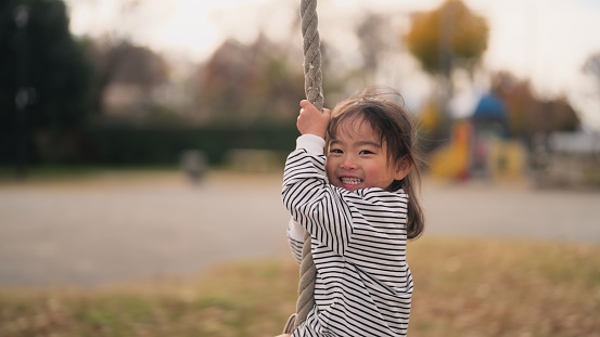 A small girl is enjoying playing with a sliding rope in a public park.