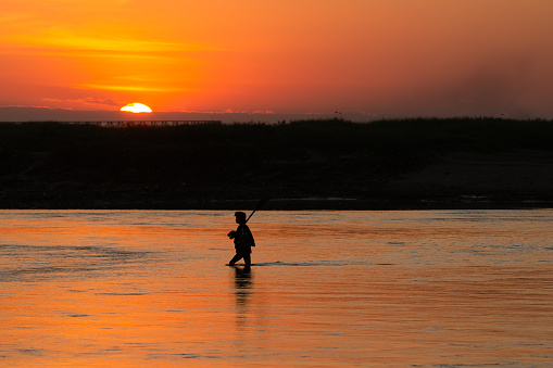 Man Walks in Front of Setting Sun Walking in Water. Beautiful reflection of a man crossing a river in front of the setting sun - Myanmar