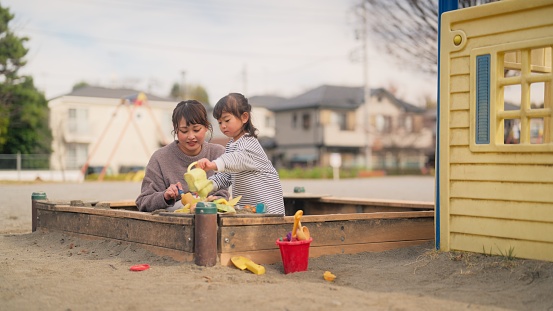 A small girl is playing with sand together with her mother in a public park.