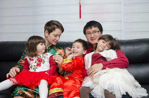 Mixed race (chinese and caucasian) mother, father, son and daughters dressed up in traditional chinese clothes for new chinese year and sitting in sofa