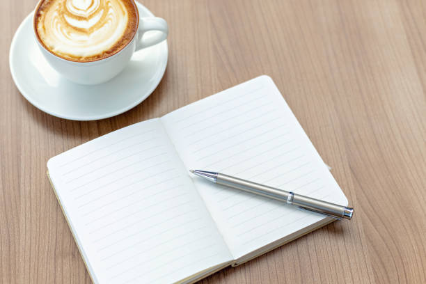 istock Open blank note pad, coffee cup and pen on wooden desk. 1458787204