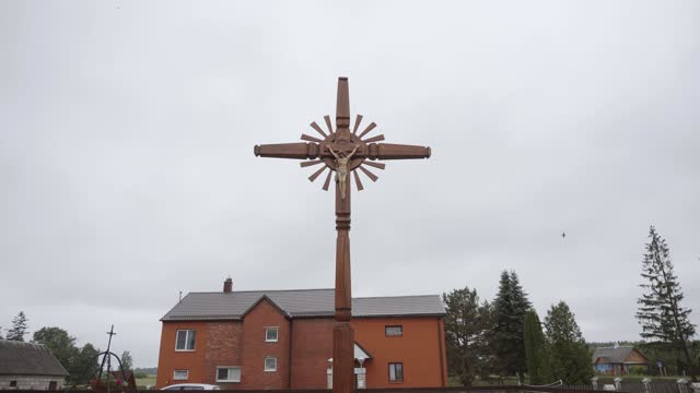 Large wooden cross with crucifixion stands in yard of church, up view.