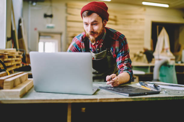 istock Creative bearded craftsman in apron working with laptop at workshop 1458787537
