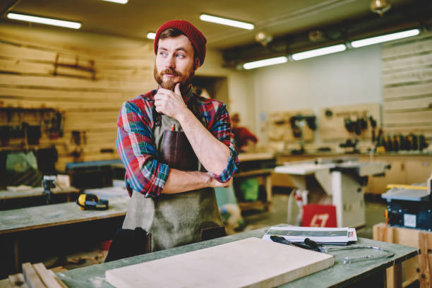 istock Bearded craftsman in apron pausing to think at workshop 1458787569
