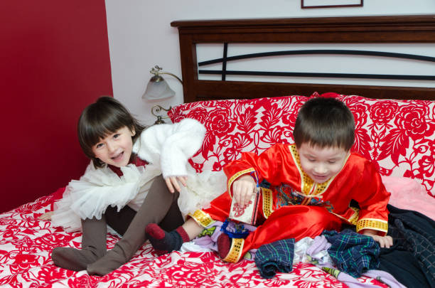 Multiracial brother and sister (Chinese and caucasian) playing on parent's bed with boy having traditional chinese clothes for chinese new year