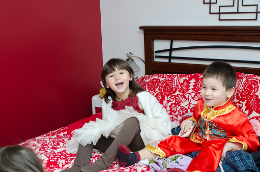 Multiracial brother and sister (Chinese and caucasian) playing on parent's bed with boy having traditional chinese clothes for chinese new year