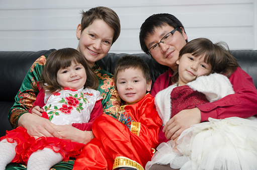 Mixed race (chinese and caucasian) mother, father, son and daughters dressed up in traditional chinese clothes for new chinese year and sitting in sofa
