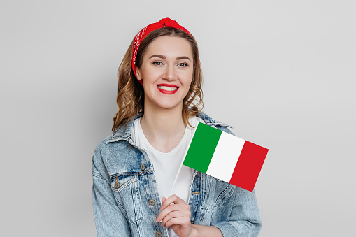 student girl smiling and holding a small Italy flag isolated on grey background in studio, copy space