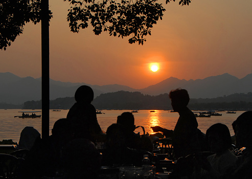 West Lake (Xi Hu) sunset in Hangzhou, Zhejiang Province, China. Sunset view of West Lake, Hangzhou with silhouettes of people sitting in a cafe.