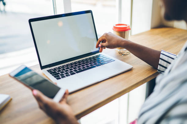 istock Black person holding smartphone and typing information on laptop 1458793010