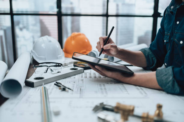istock Engineering working with drawings inspection on tablet in the office and Calculator, triangle ruler, safety glasses, compass, vernier caliper on Blueprint. Engineer, Architect, Industry and factory concept. 1458793598