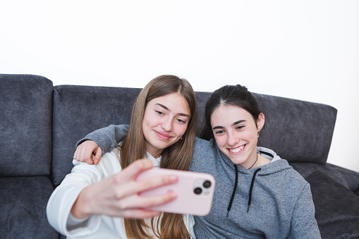 Portrait of two happy teenage girls taking a selfie at home interior. Enjoying talks, having fun. Happy tech lifestyle concept.