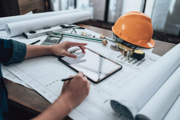 istock Engineering working with drawings inspection on tablet in the office and Calculator, triangle ruler, safety glasses, compass, vernier caliper on Blueprint. Engineer, Architect, Industry and factory concept. 1458799803